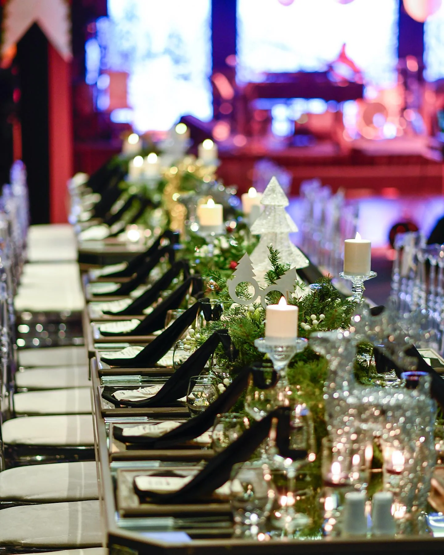 Christmas Gala: Masanın ucundan salona bakış: sıralanmış altın ağaç figürleri, siyah peçeteler ve arkada aydınlatılmış sahne