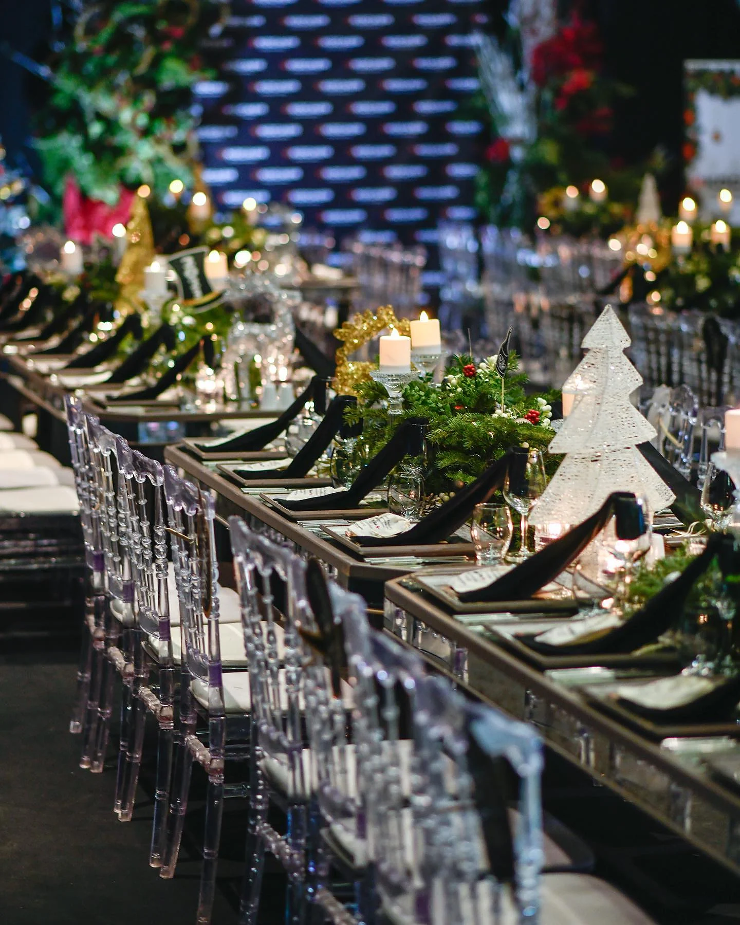 Christmas Gala: Şeffaf sandalyelerle uzayan masa dizisi; yeşillik şeridi ve beyaz ağaç figürleri