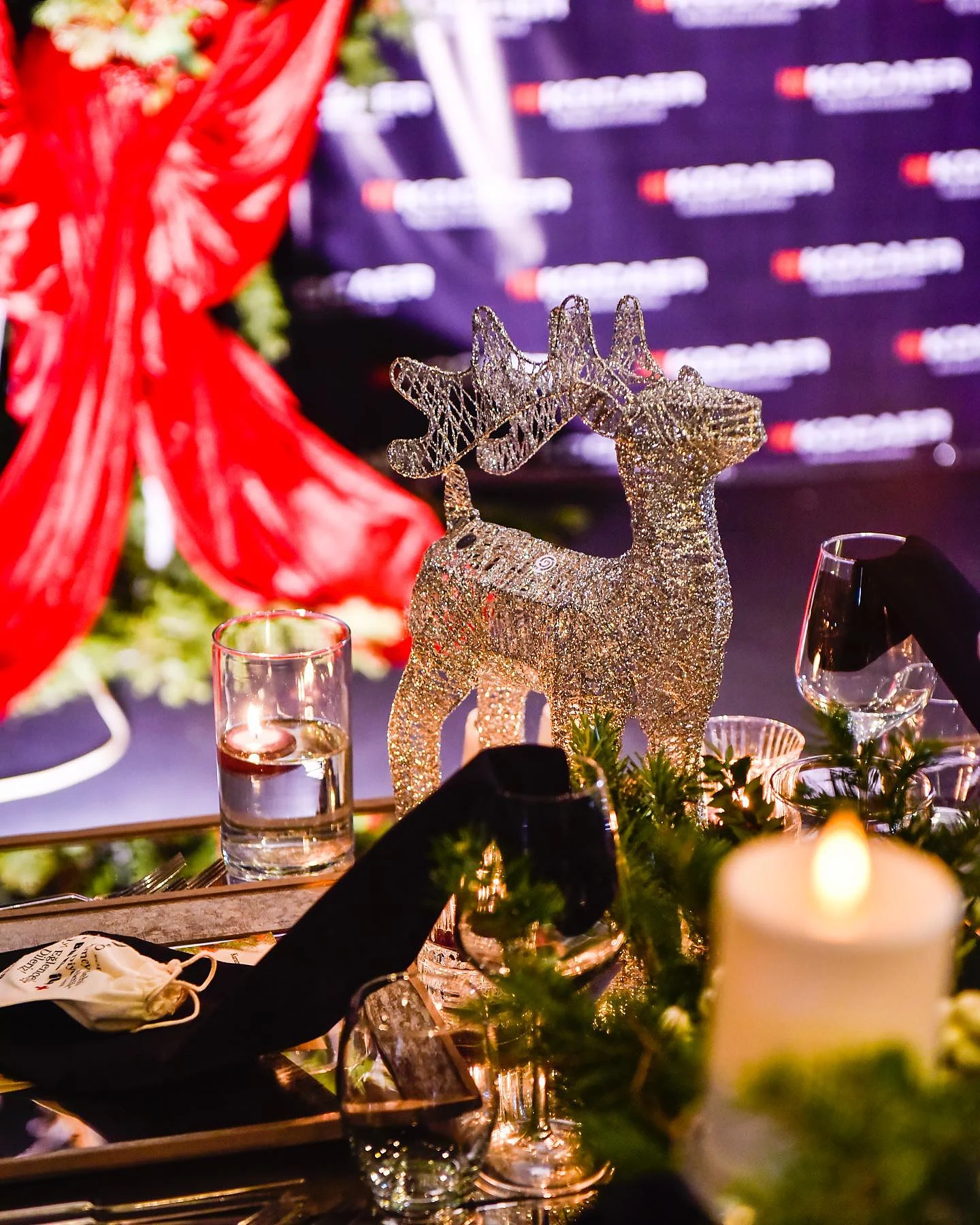 Christmas Gala: Altın tel geyik figürü yakın planda; arkada kırmızı drape, önünde mum ve bardaklar