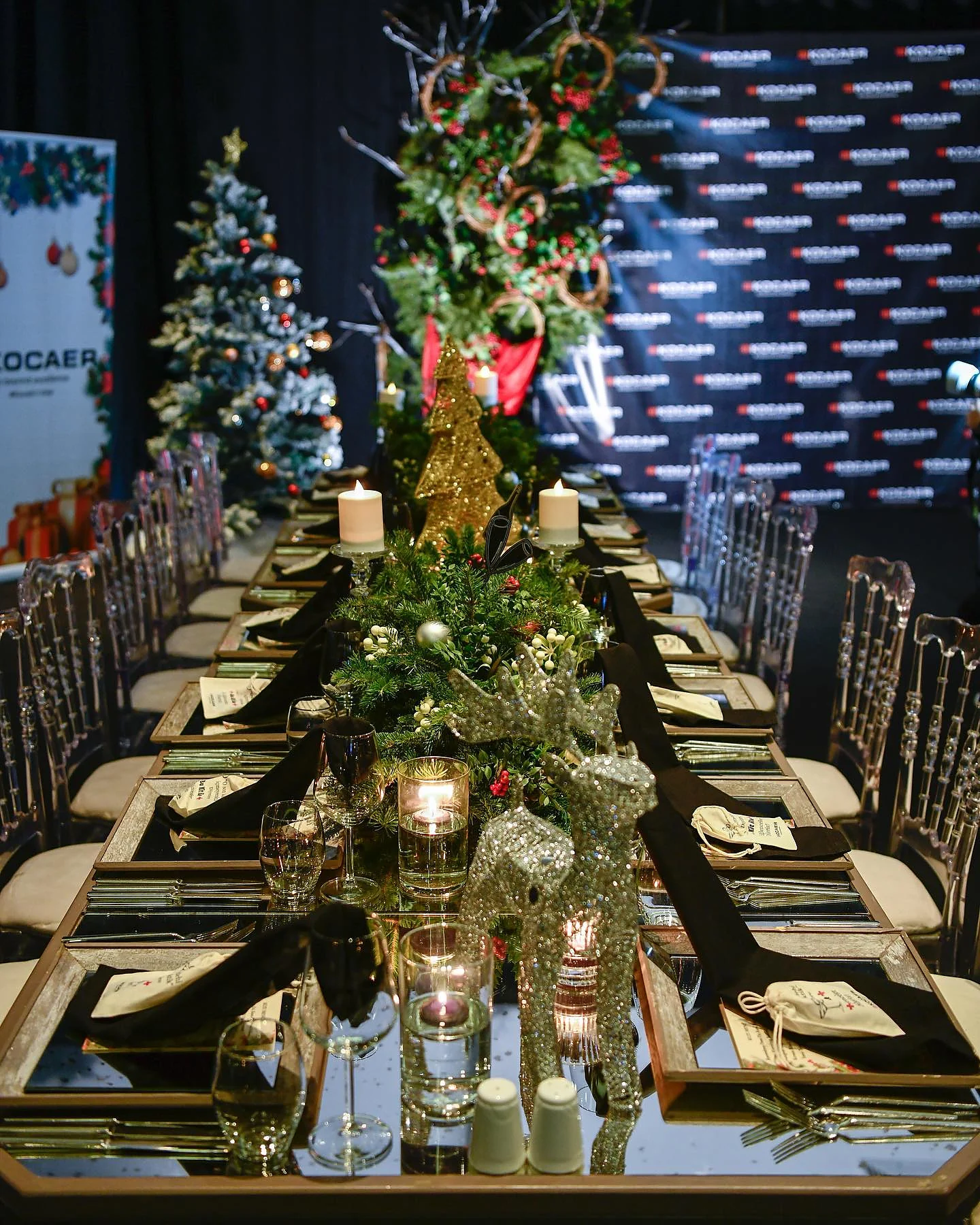 Christmas Gala: Masanın ortasında yeşillik ve mum kompozisyonu; solda süslenmiş yılbaşı ağacı