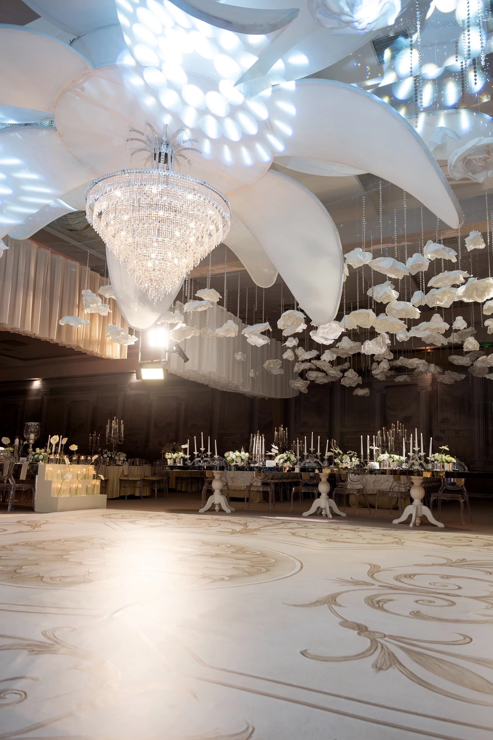 Kristal avize, asılı beyaz çiçekler ve uzun aynalı sofralarla salon görünümü