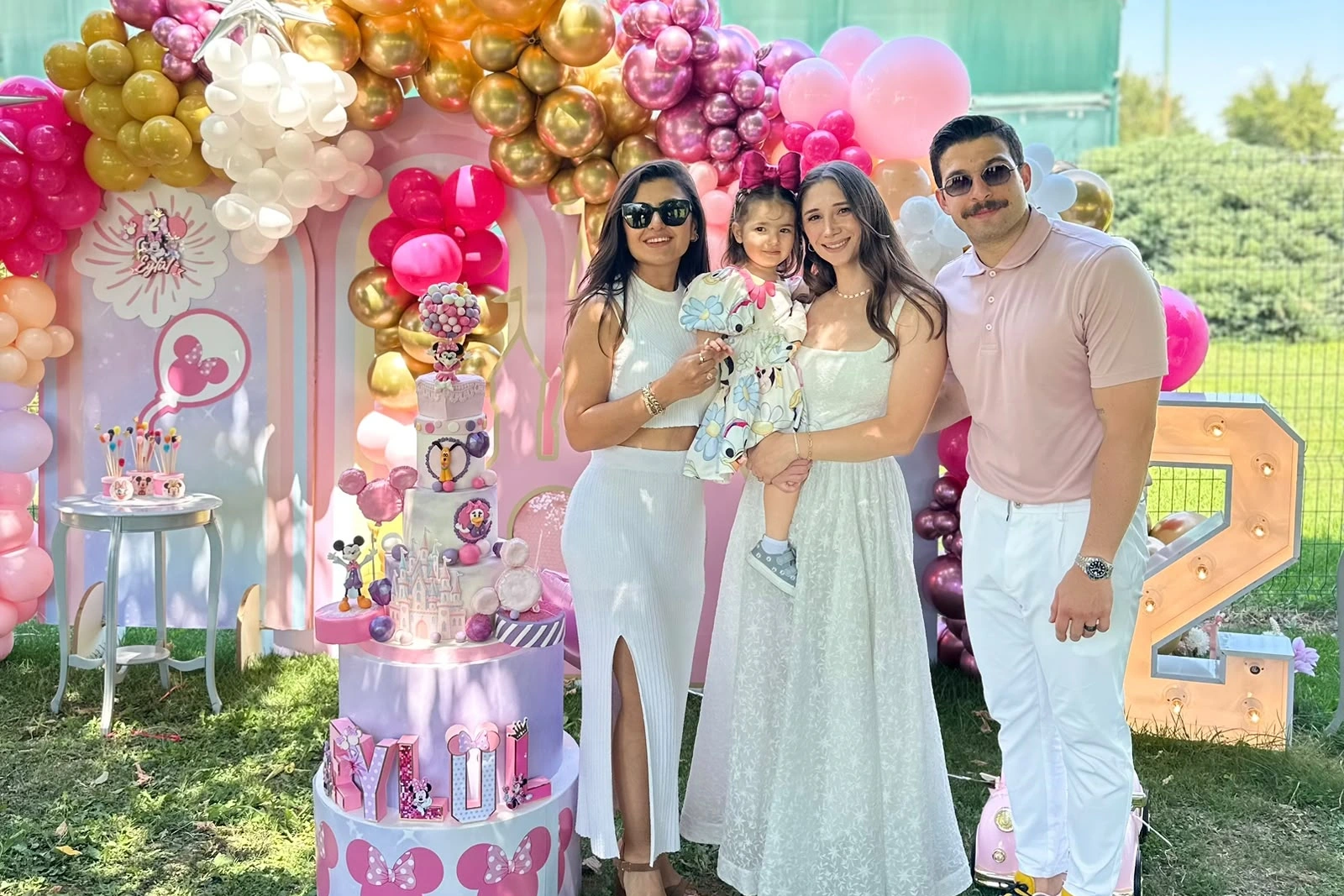 Pembe ve altın Minnie dekoru önünde aile portresi