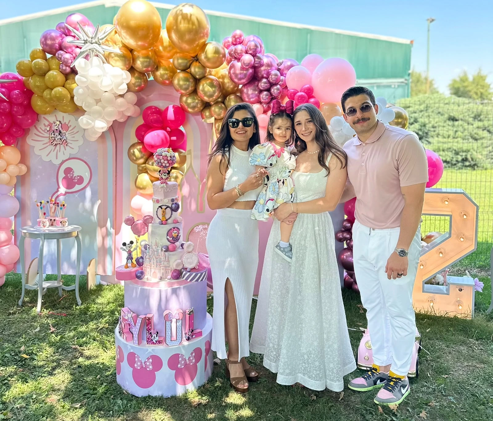 Pembe ve altın balonlu Minnie sahnesi önünde aile portresi