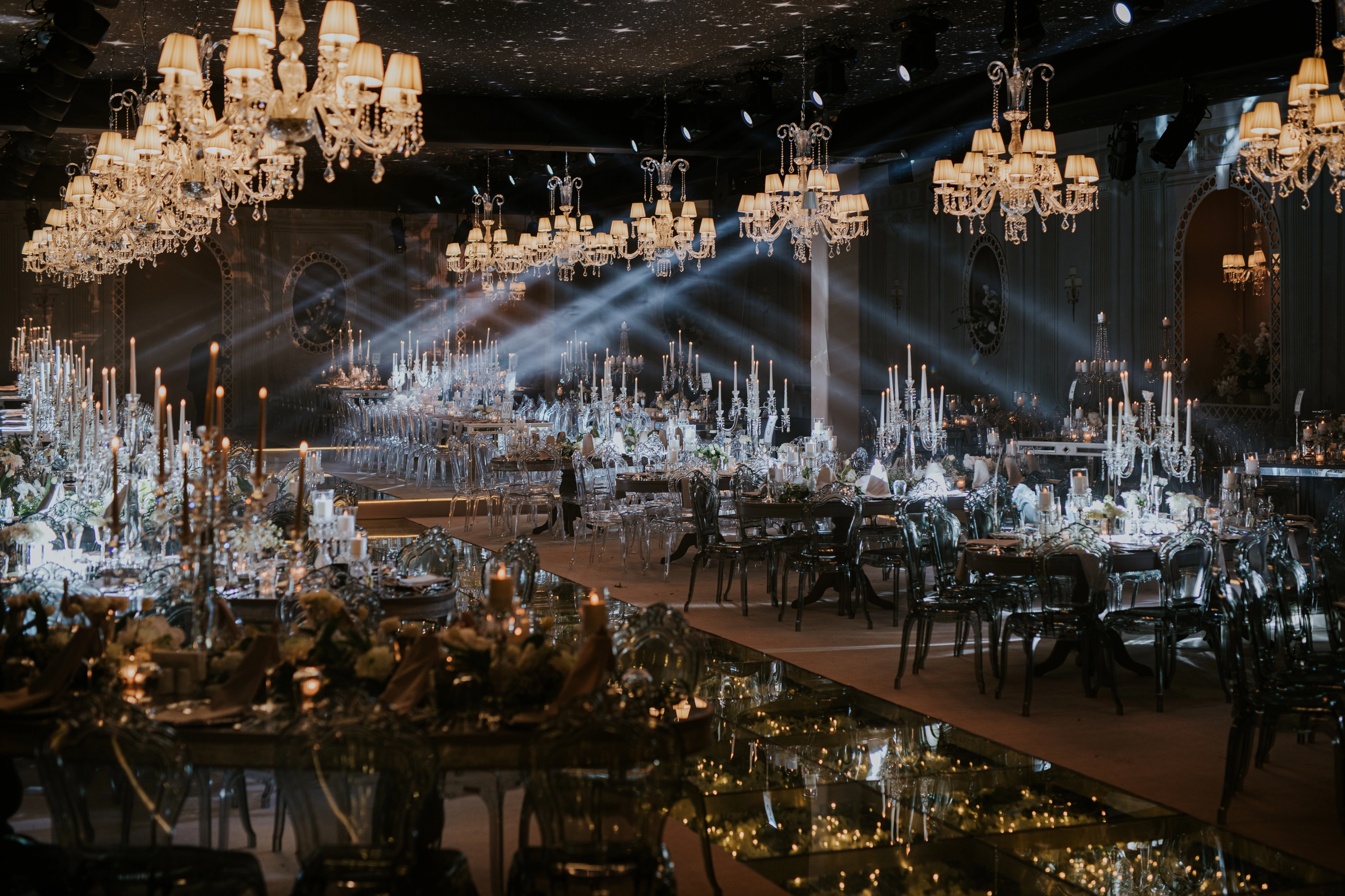 Evening ballroom with beams of light, crystal chandeliers and long tables