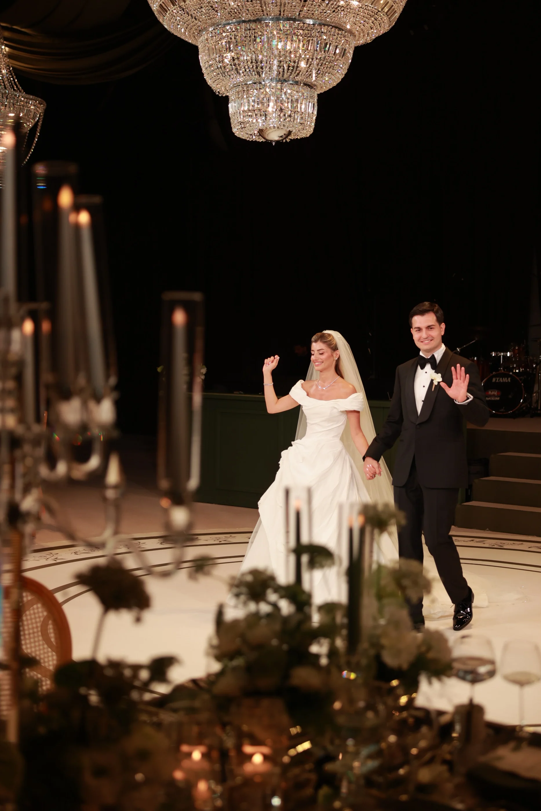 Kristal avizeler ve mum ışığı arasında yürüyen gelin ve damat